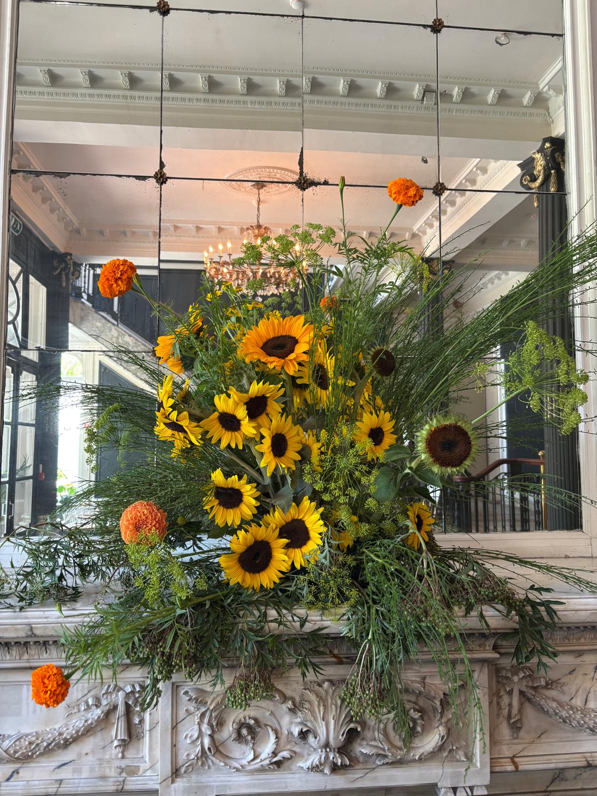 Groot bloemstuk met zonnebloemen, afrikaantjes en dille voor een antieke spiegel